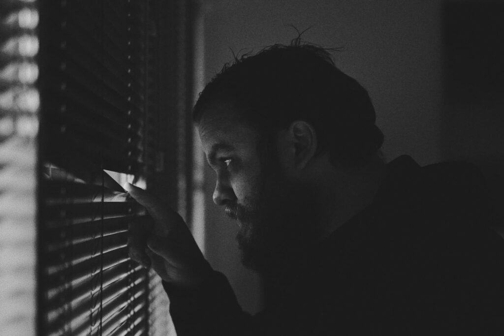 Man peeping out of a window with the blinds closed