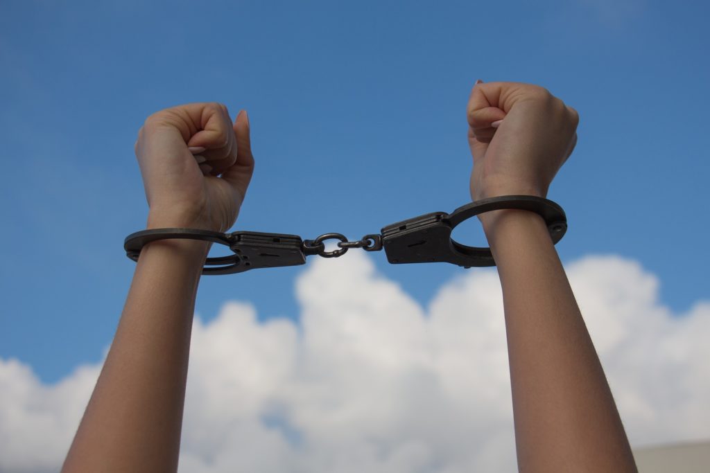 Person’s wrists in handcuffs against sky