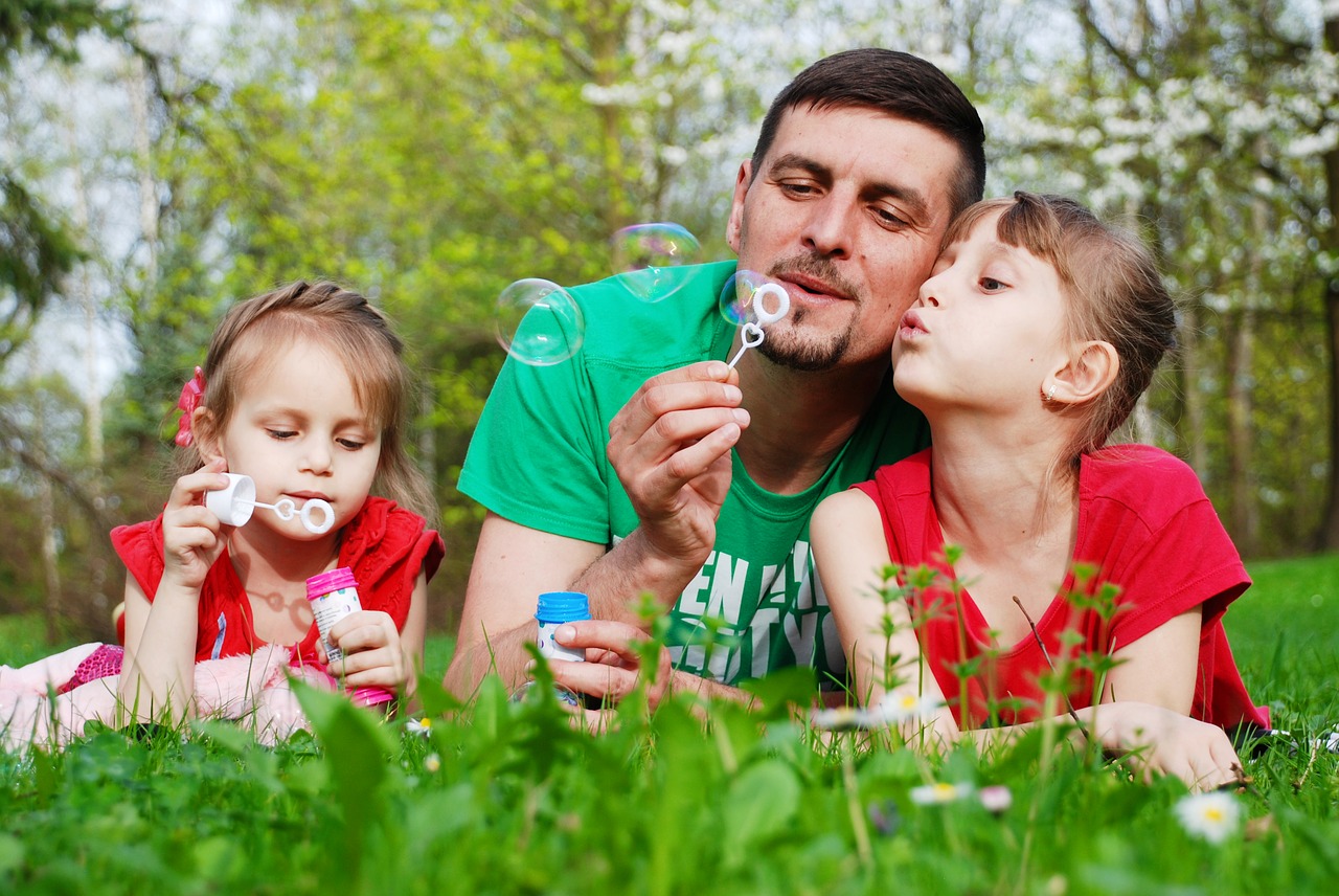 Father blowing bubbles in the grass with two young daughters 