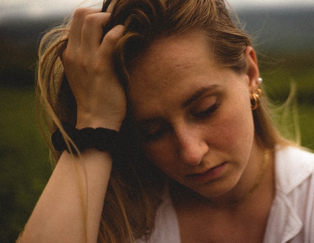 Photo of a woman with hand on her forehead looking down and looking tired or upset